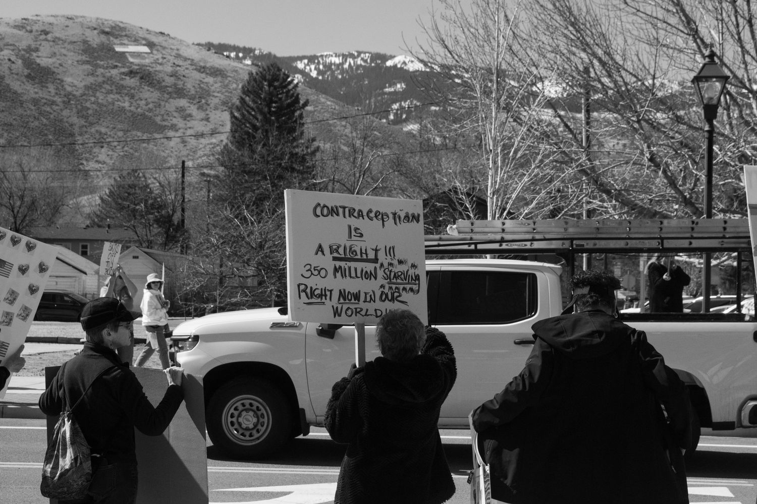 Black and white photo of protesters holding a detailed contract plan sign at an outdoor political demonstration.