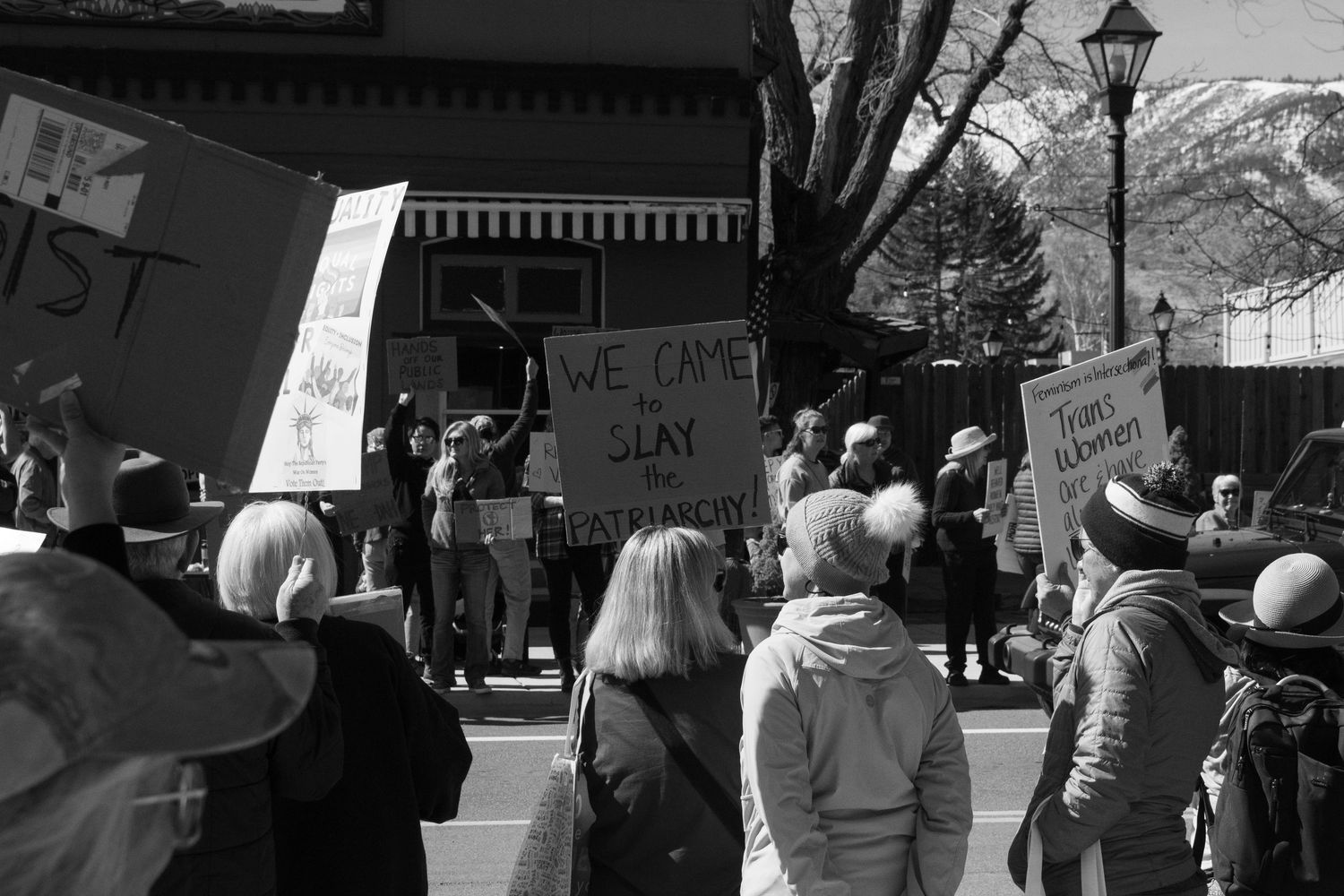 Black and white photo of protesters holding signs at an outdoor rally with mountains visible in the background.