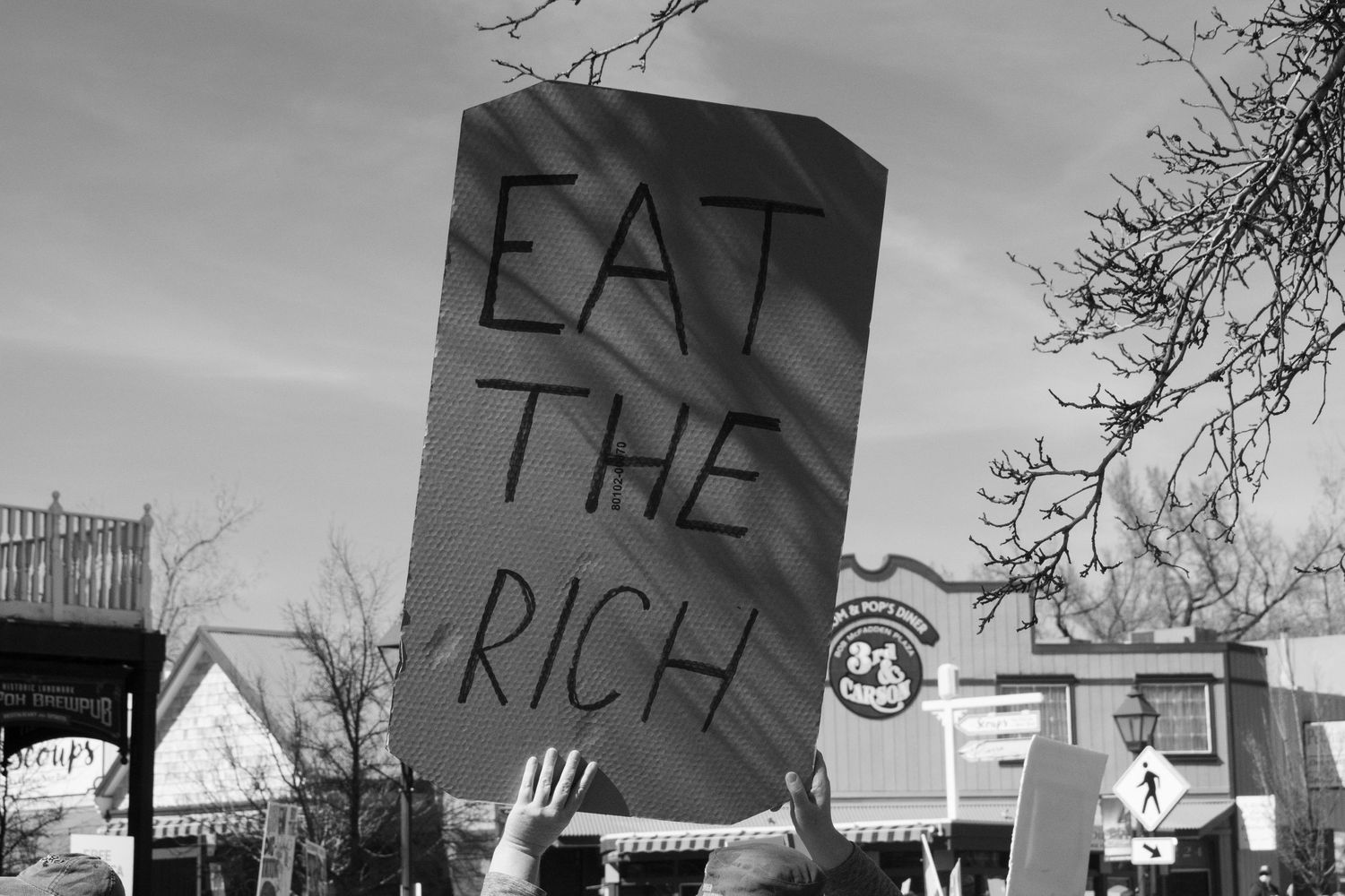 Protester holds a handmade cardboard sign reading Eat The Rich at an outdoor demonstration.