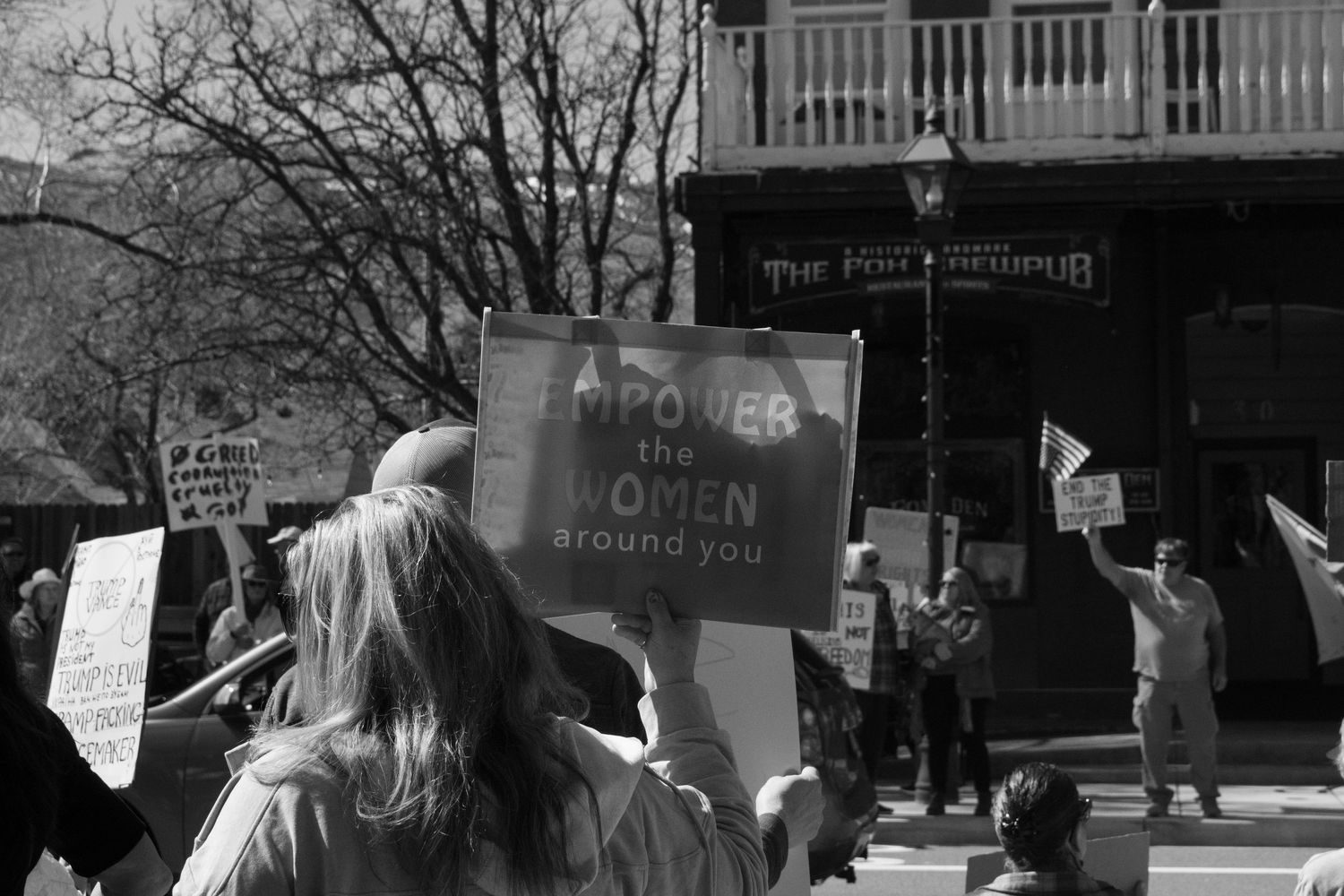 Black and white image of protesters holding signs including Power the Women Around You at a street rally.