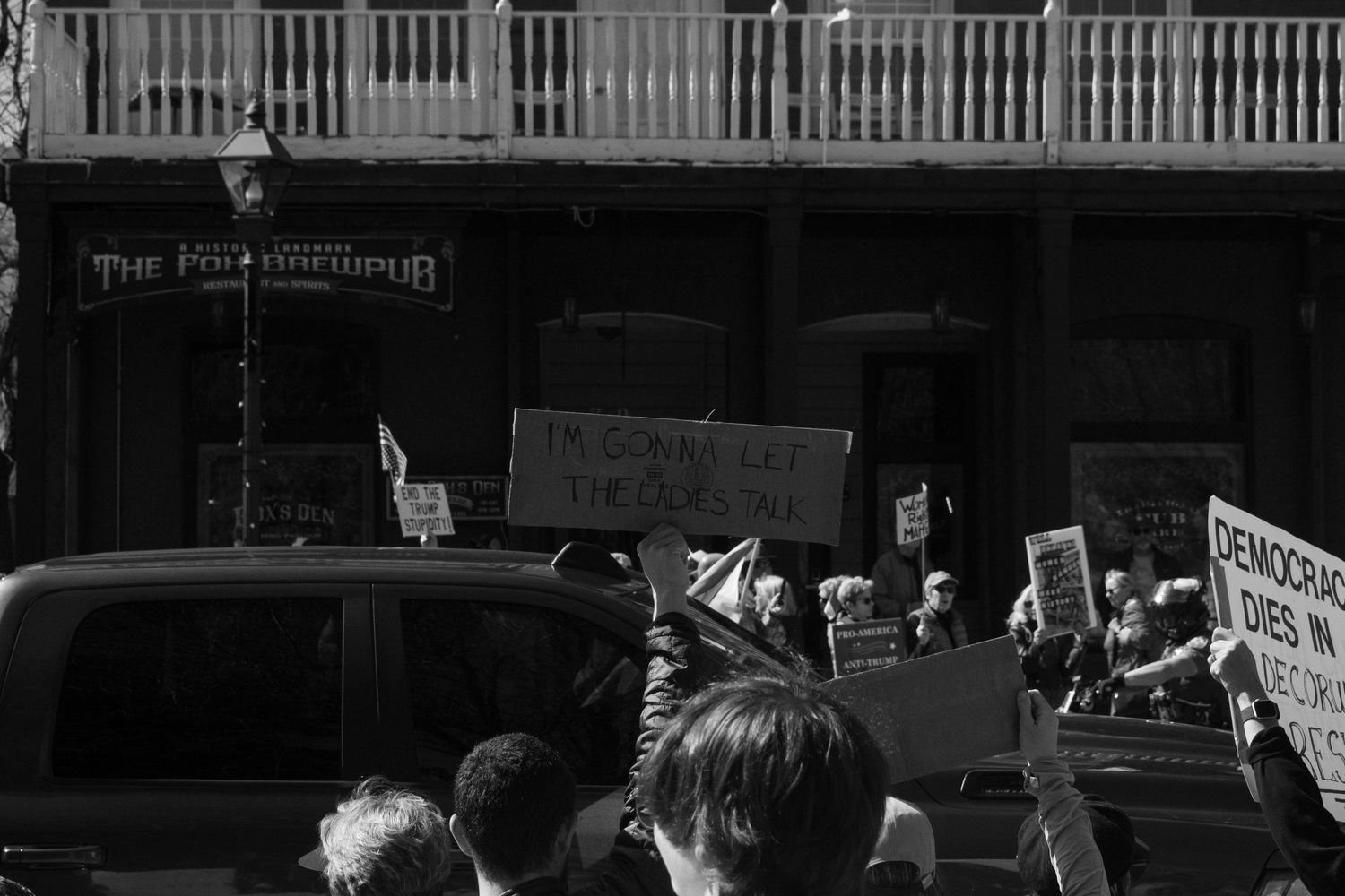 Crowd of protesters with signs gathered outside The Pontchartrain Pub during a street demonstration.
