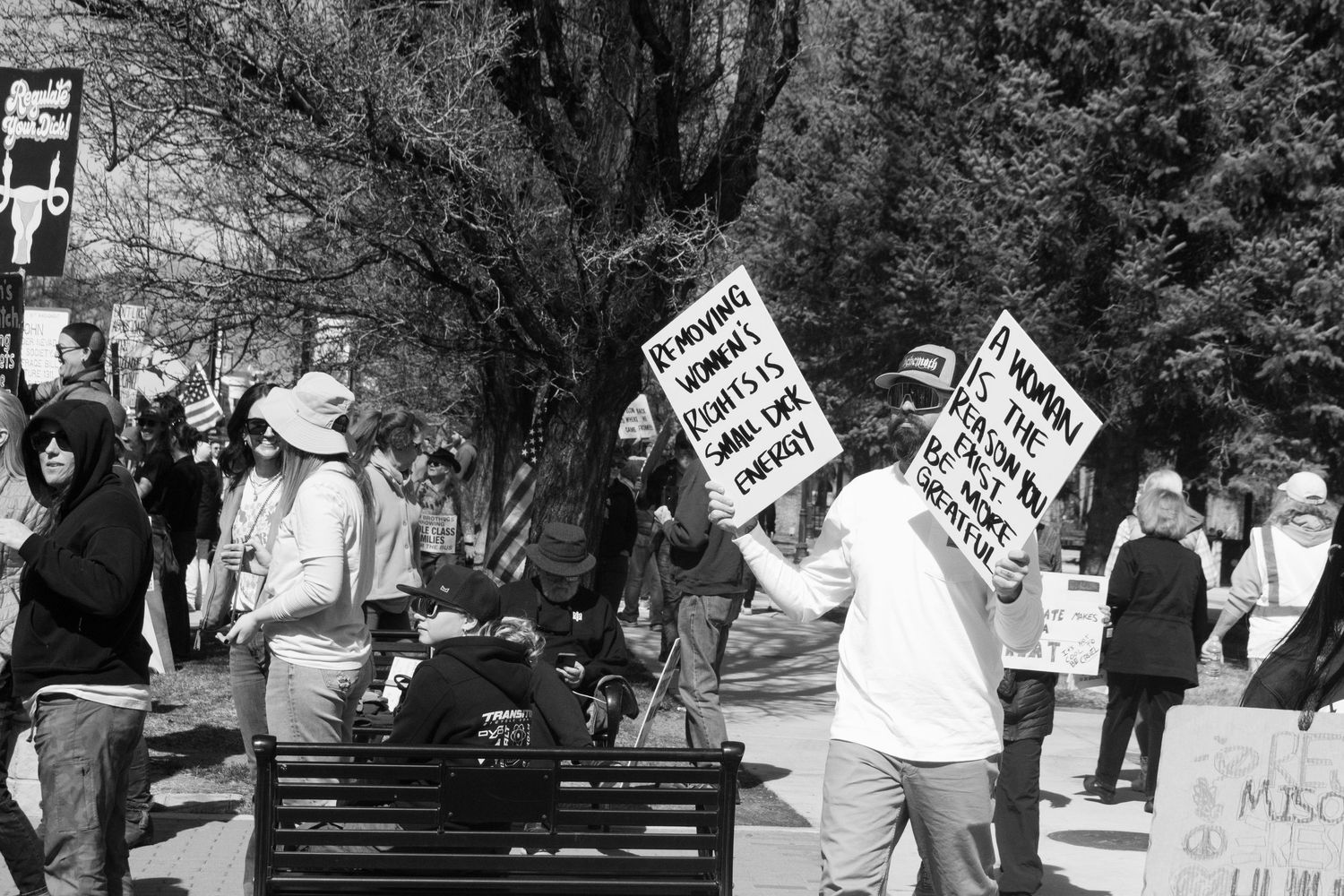 Protesters march along a tree-lined street holding signs about womens rights at a public rally.