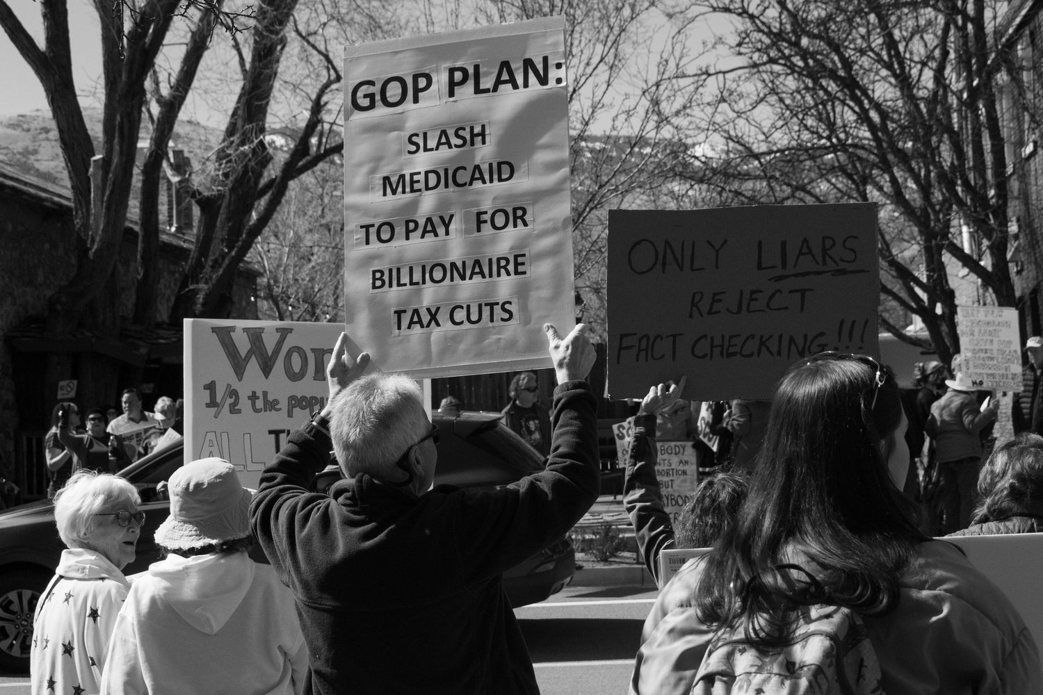 Protesters hold signs reading GOP Plan Slash Medicaid To Pay For Billionaire Tax Cuts at demonstration.