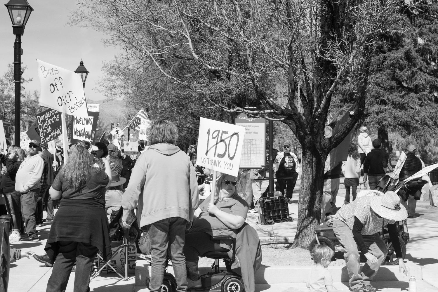 Large group of protesters gather outdoors holding various signs including one reading 1950 at rally.