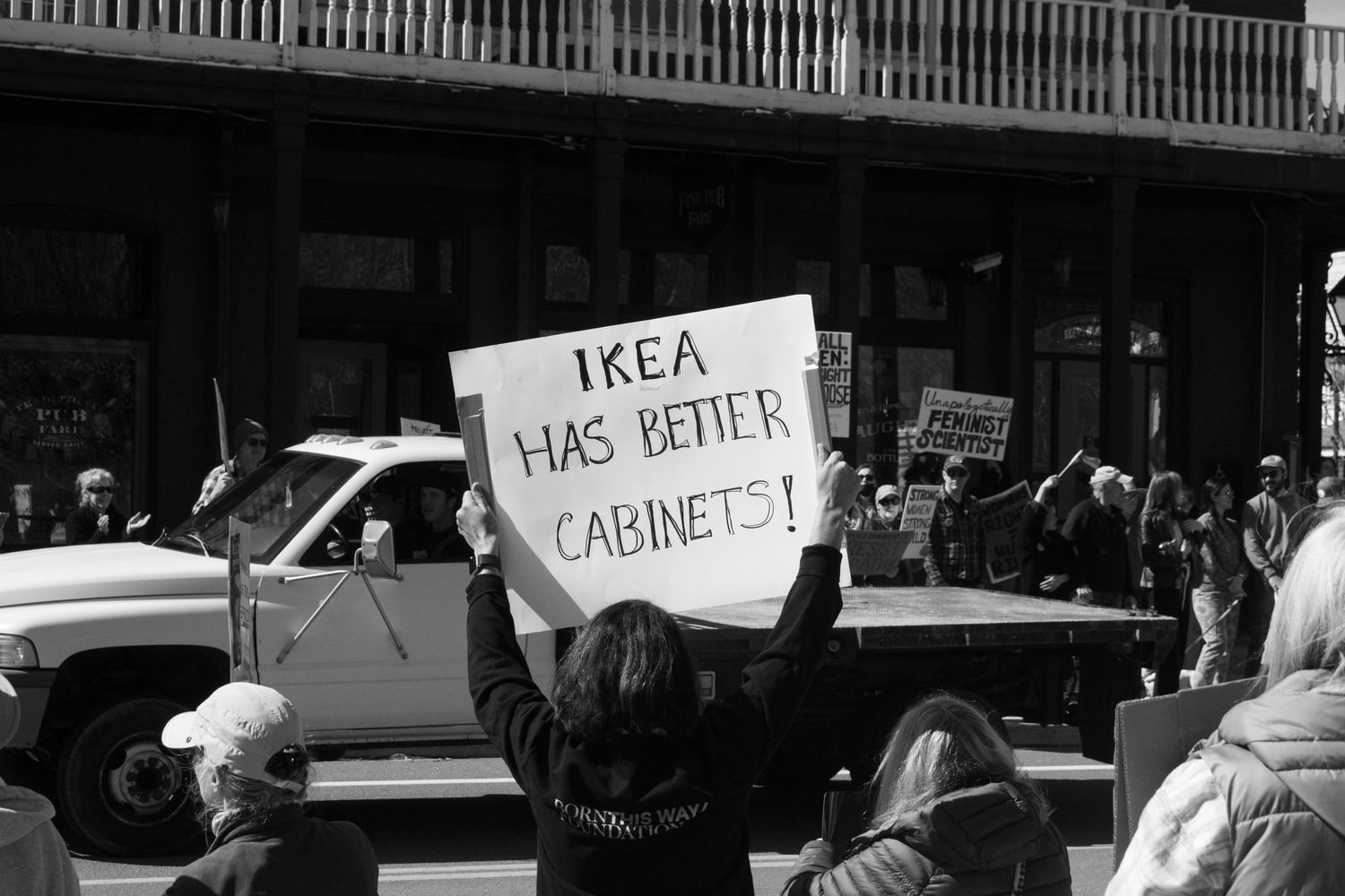 Protester holds sign reading IKEA Has Better Cabinets at black and white outdoor political demonstration.