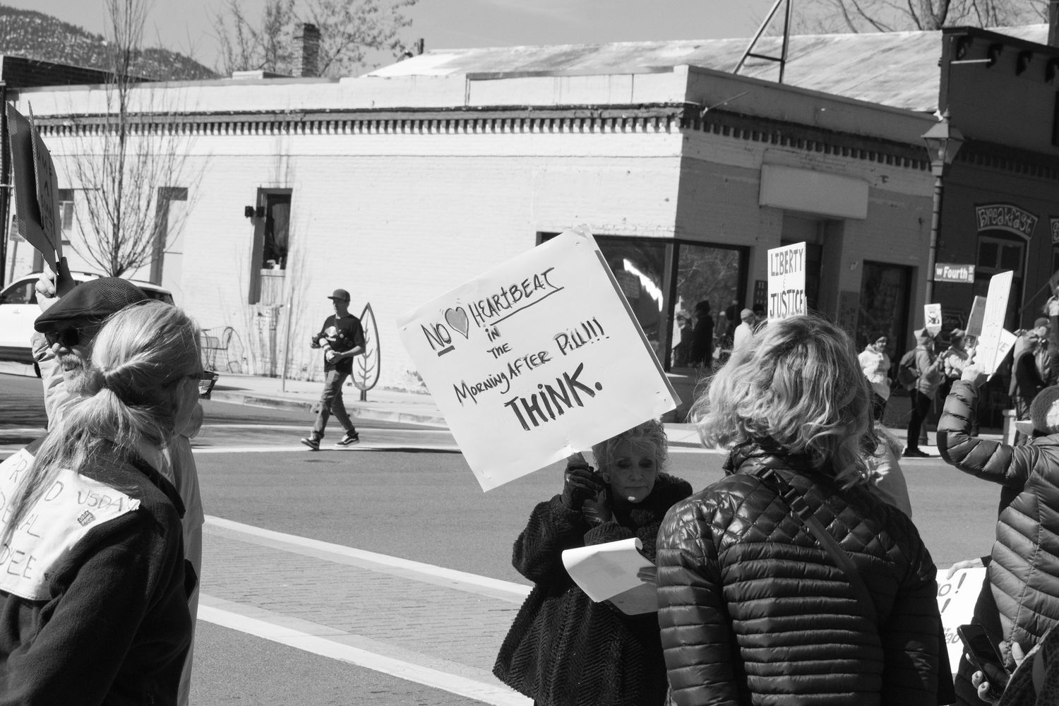 Protesters hold signs including one about democracy at black and white outdoor political demonstration.