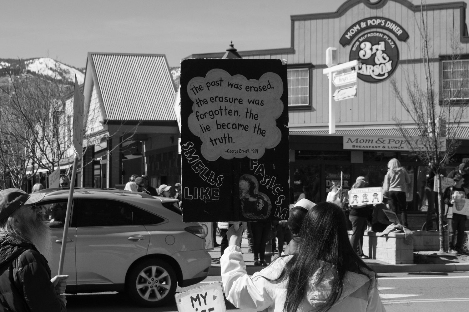 Protester holds dark sign with quote about past erasure at black and white street demonstration.