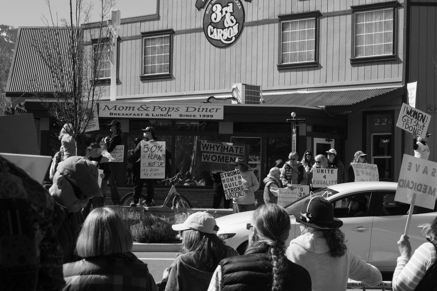Black and white photo of protesters holding signs outside Mom and Pops Diner during a public demonstration.