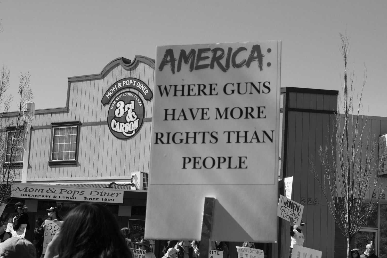 Protest sign reading America Where Guns Have More Rights Than People at a public rally.