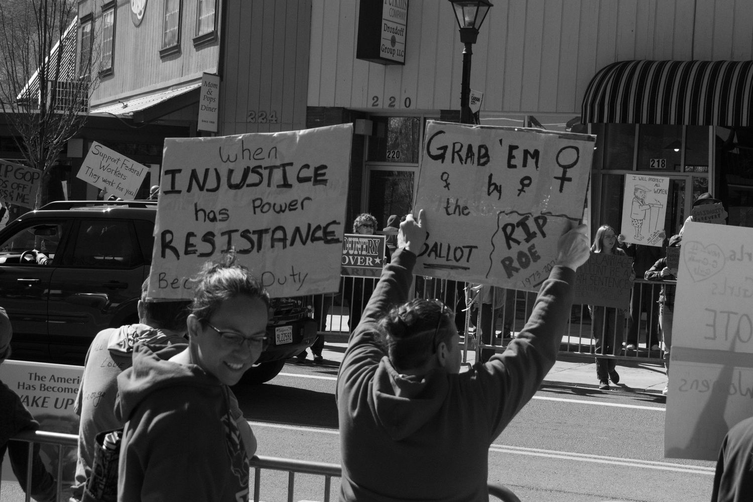Protesters holding signs including When Injustice Becomes Power Resistance and Grab Em at a rally.