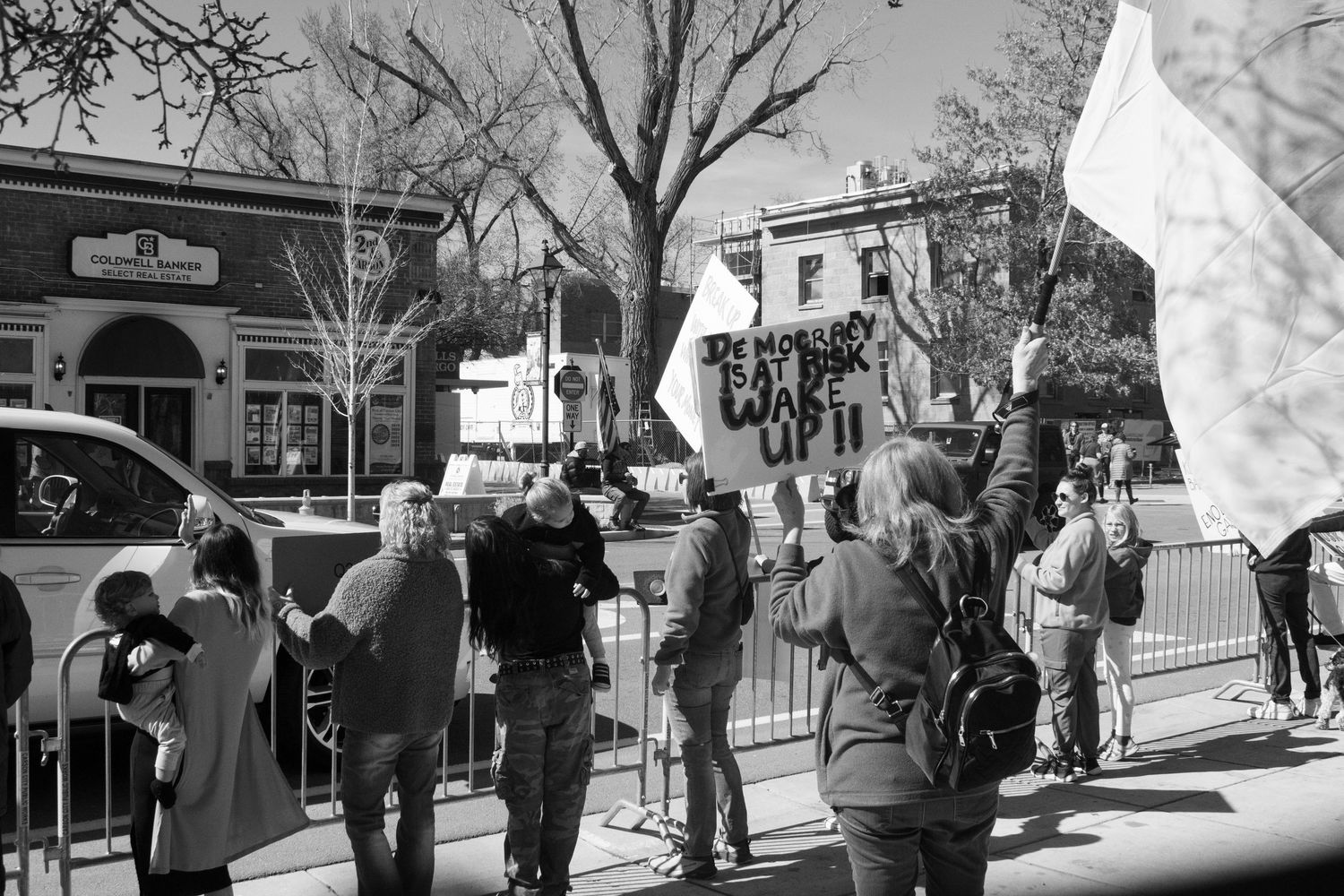 Black and white image of demonstrators holding signs and flags at an outdoor protest rally.