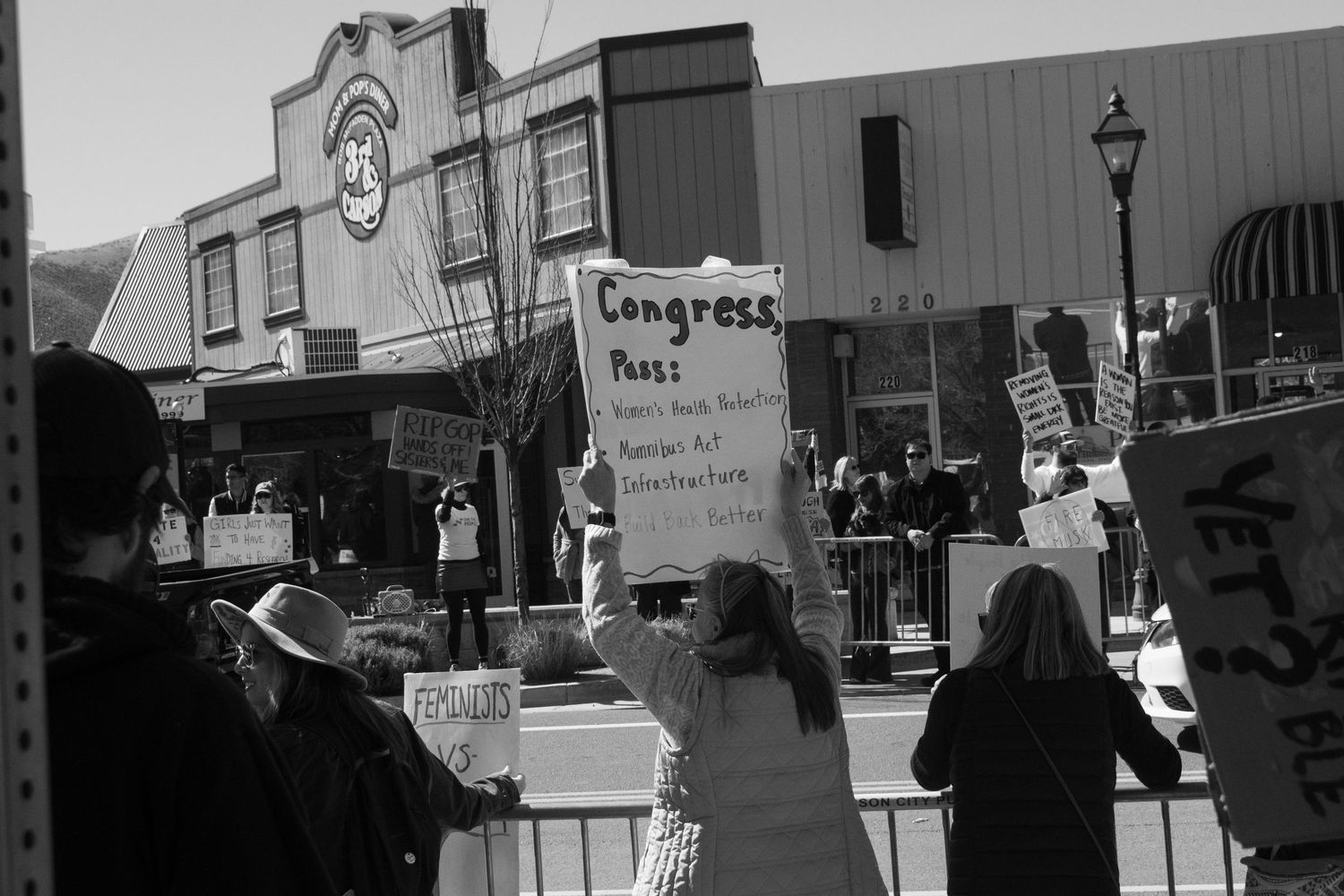 Protester holds sign addressed to Congress at an outdoor political demonstration in black and white.