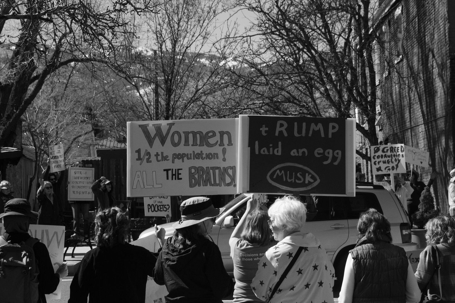 Black and white protest photo featuring signs reading Women Half the Population and Trump Laid an Egg.