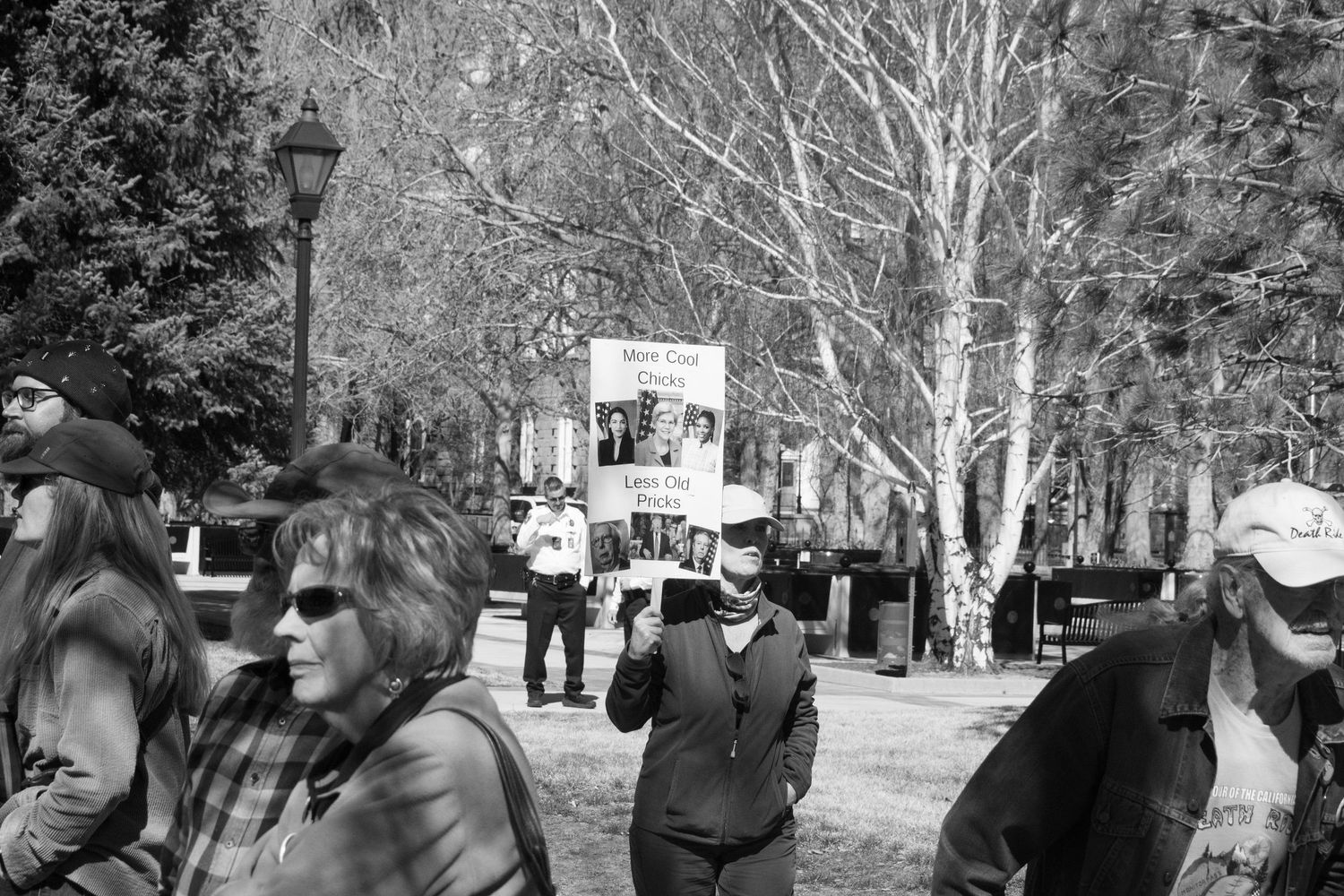 Black and white photo of people gathered in a tree-lined park during a protest rally outdoors.