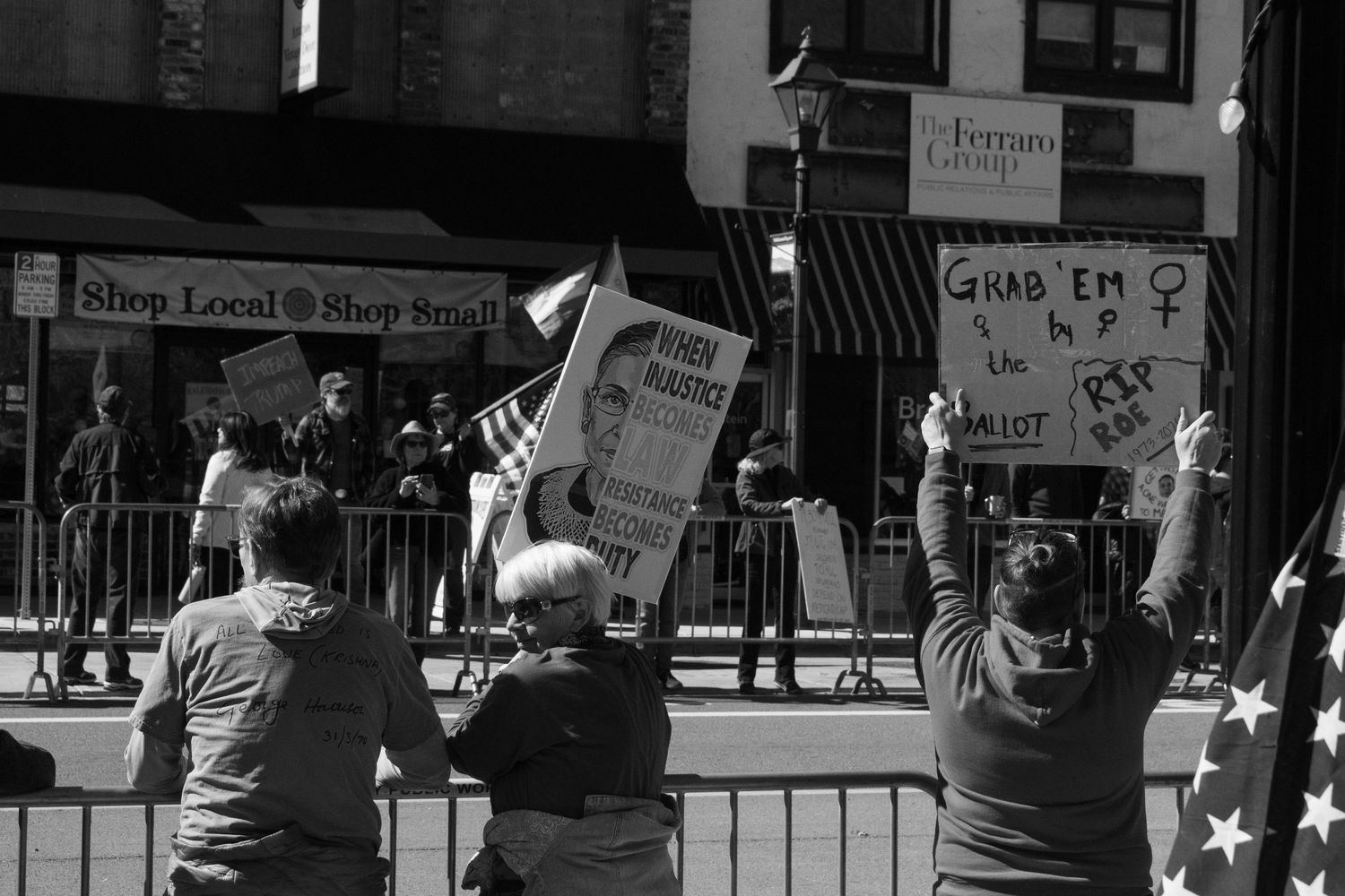 Black and white photo of protesters outside shops holding signs including Grab Em at a street rally.