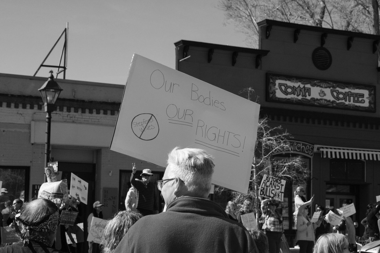 Black and white photo of a protester holding a sign reading Our Bodies Our Rights at an outdoor rally.