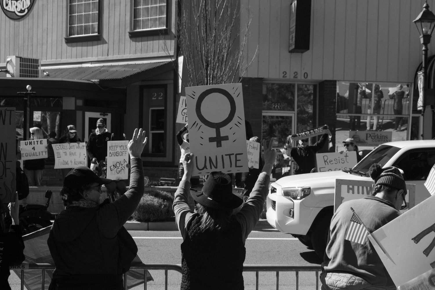 Protesters holding Unite sign with female symbol at outdoor rally in black and white.