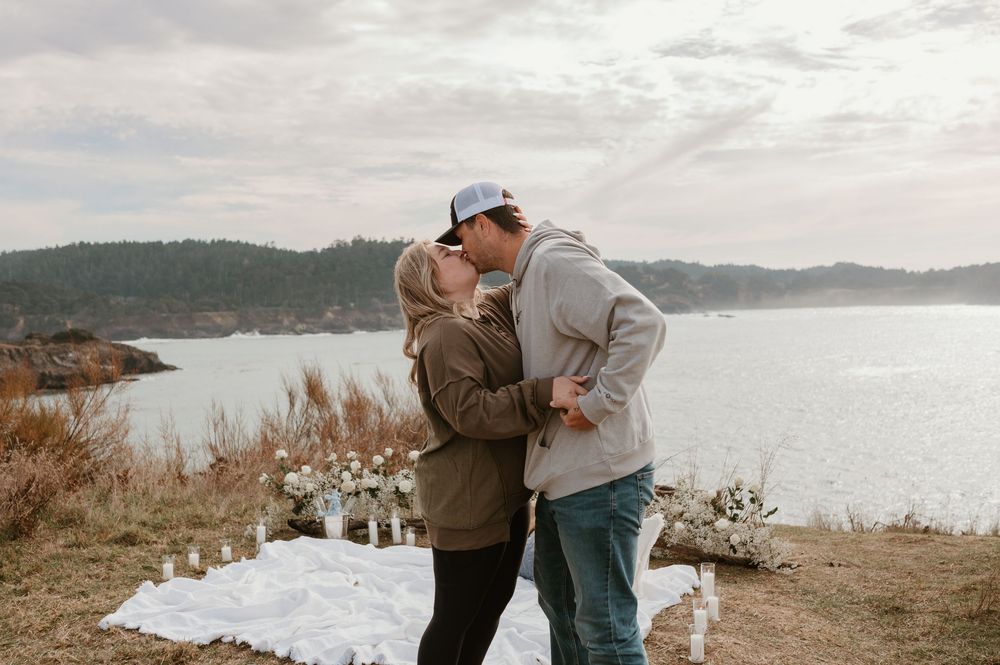 Two people share an emotional moment on a coastal cliff decorated with white flowers.