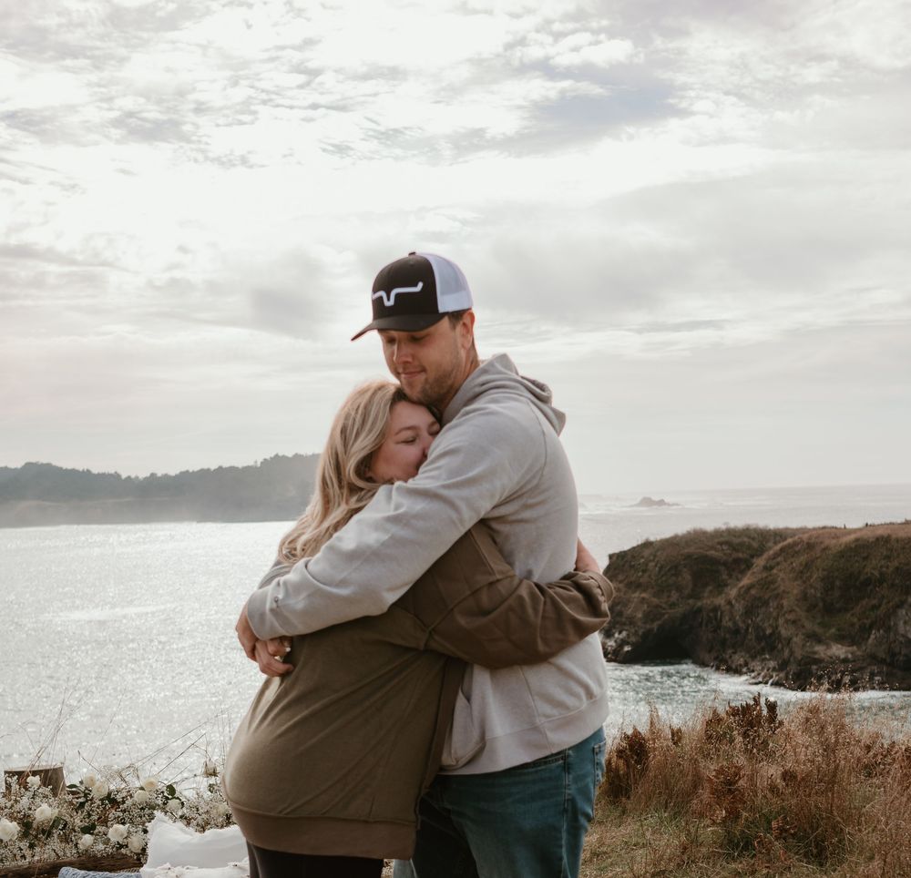 Couple sharing an intimate moment on a coastal clifftop with ocean views in the background.