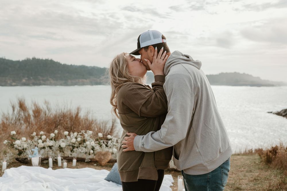 Romantic embrace on a scenic overlook with water and mountains in the distance.