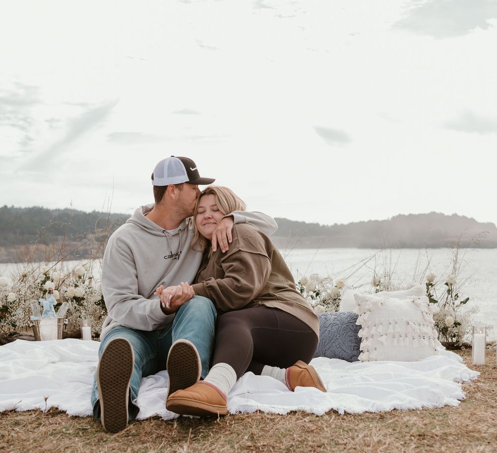 Couple relaxing together on a blanket by the water's edge during an overcast day.