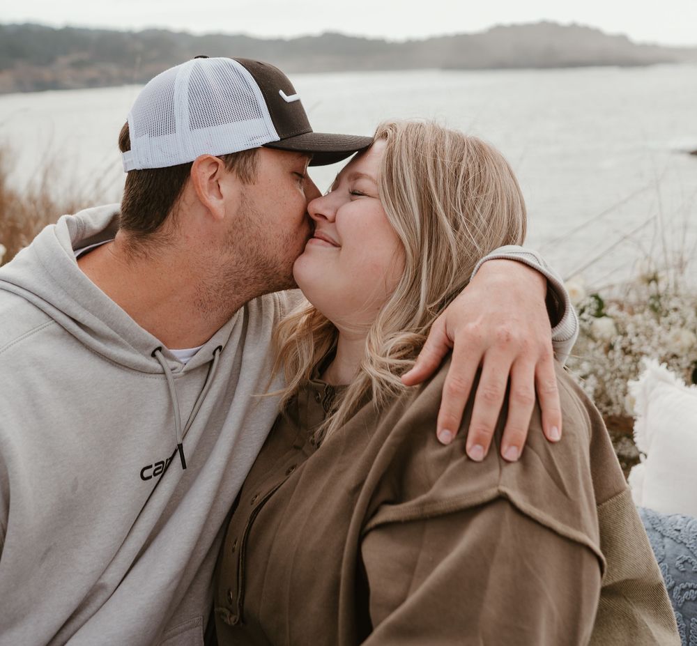 Tender moment captured between two people against a scenic coastal backdrop.