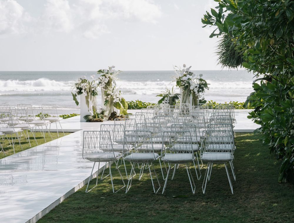 White chairs arranged for an outdoor beach wedding ceremony with floral arrangements and ocean waves in the background at Bali Beach