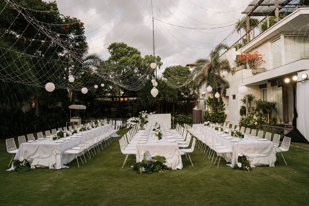 Elegant outdoor wedding reception setup with round tables under string lights in a lush garden setting in Bali.