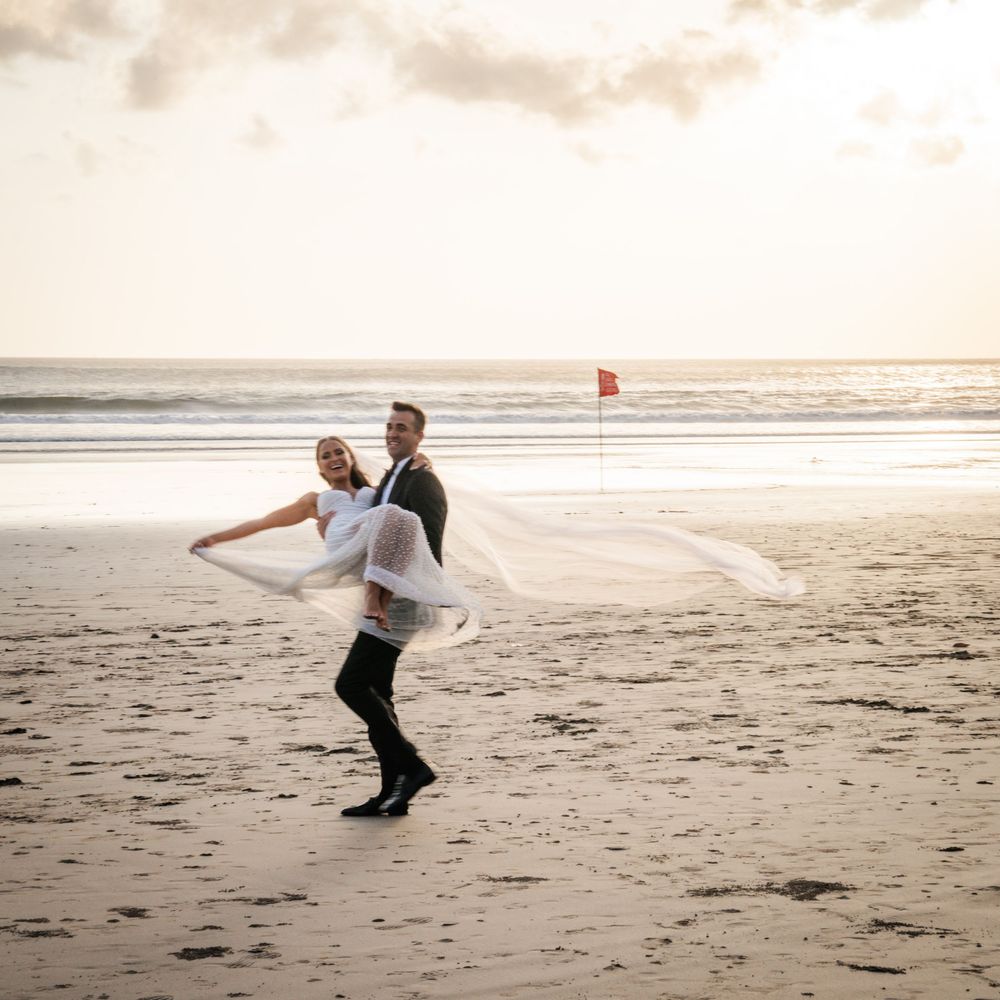 Two figures dancing playfully together on a sandy beach at golden hour during sunset in Bali