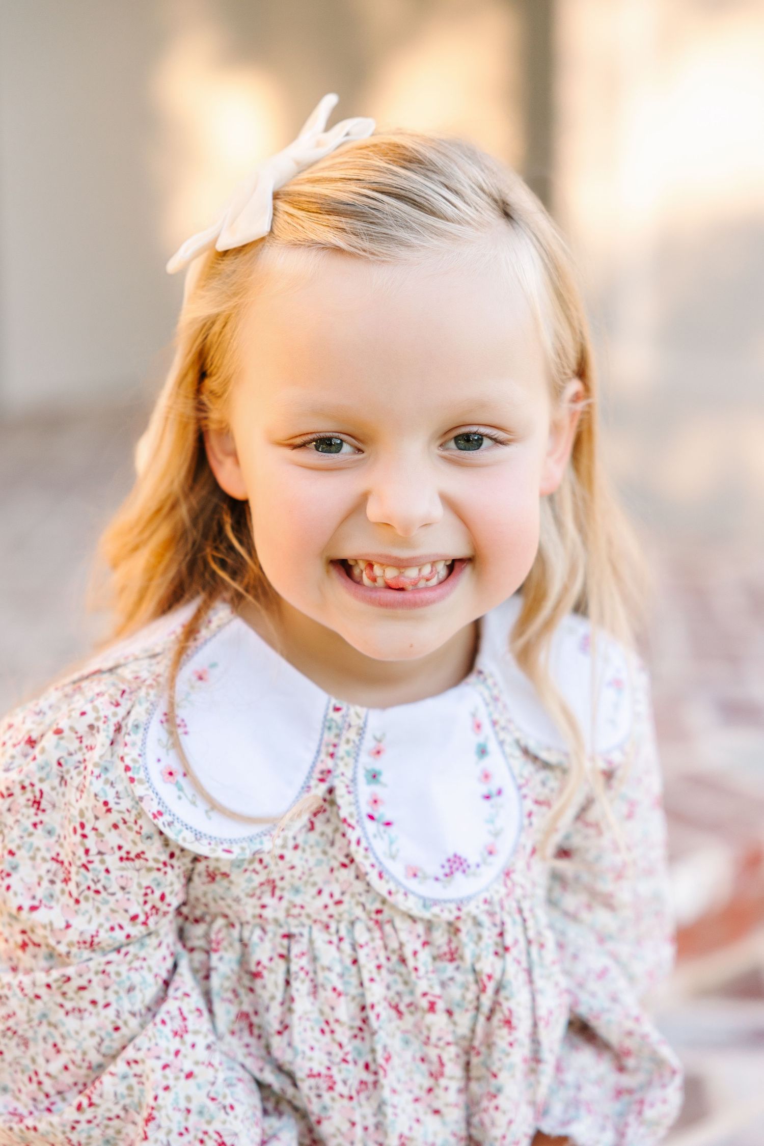 Adorable child in floral dress with white Peter Pan collar smiles brightly in outdoor portrait series.