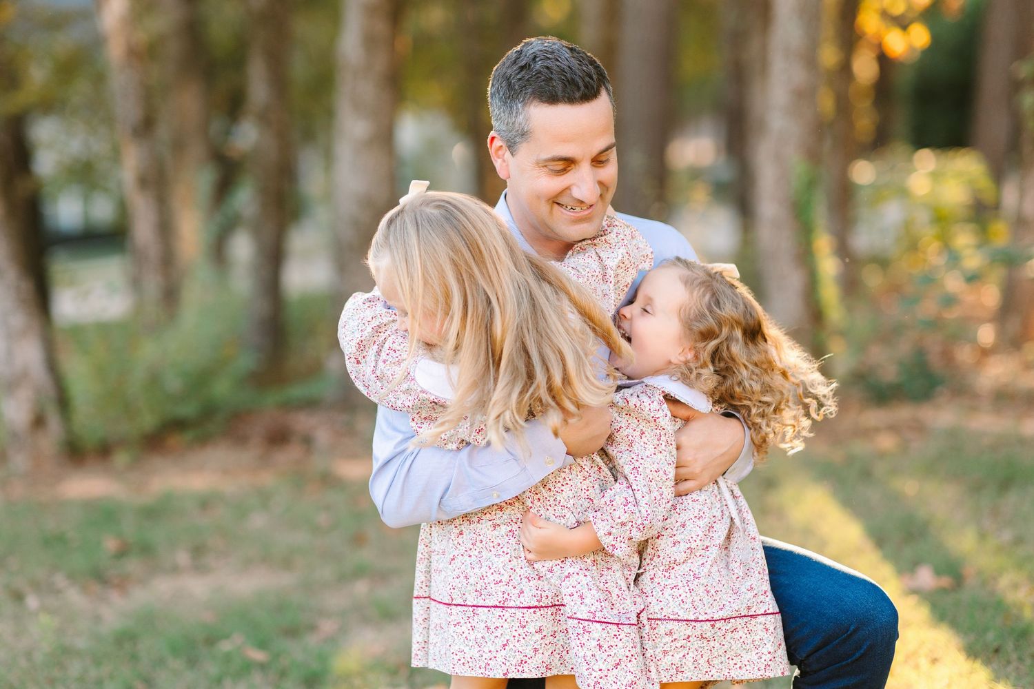 Family in coordinating pink and blue outfits taking portraits in a sunlit forest setting during golden hour.
