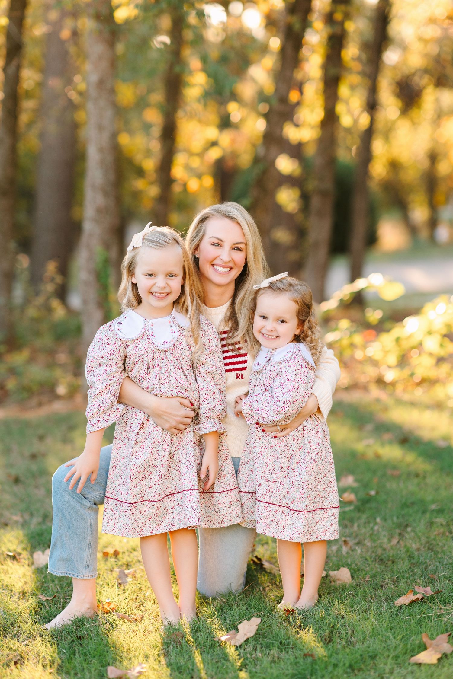 Golden sunlight illuminates a family portrait session with matching pink floral outfits in an autumn forest setting.