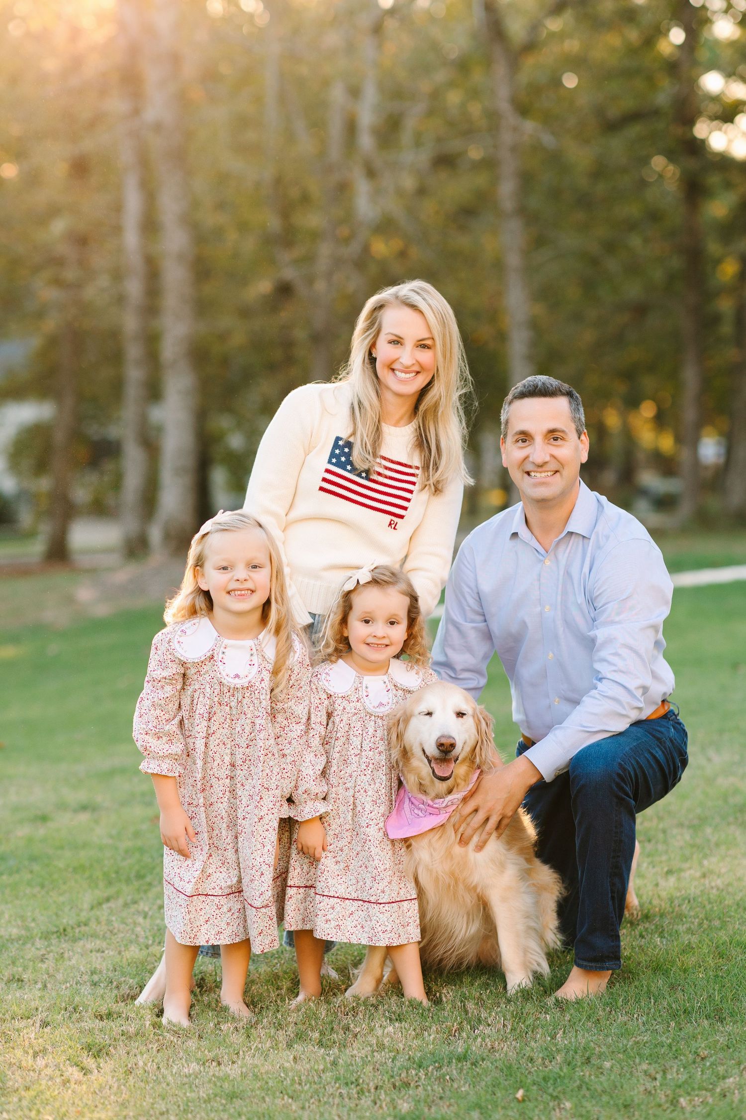 Family poses outdoors with golden retriever dog during fall sunset among trees.