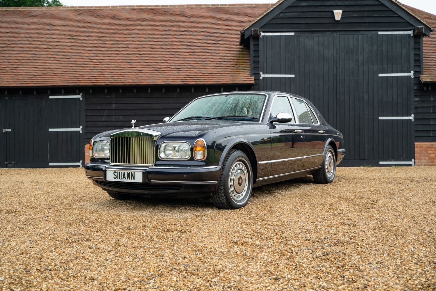 Luxury vehicles parked in front of black barn with gravel driveway.