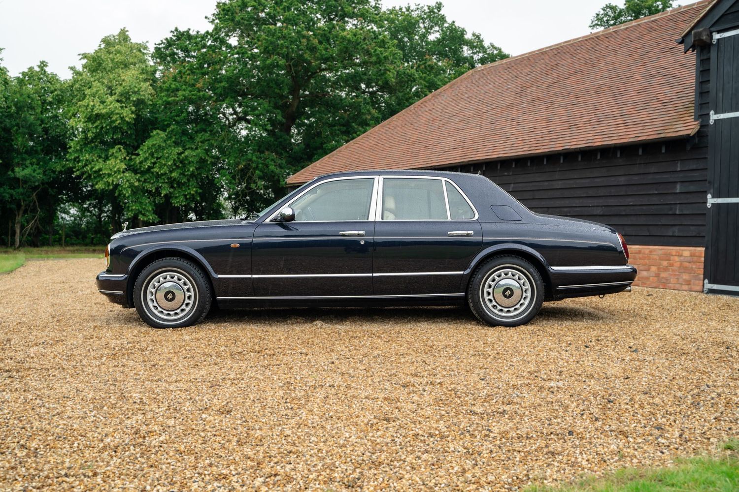 Classic luxury cars lined up outside black barn with brown roof.