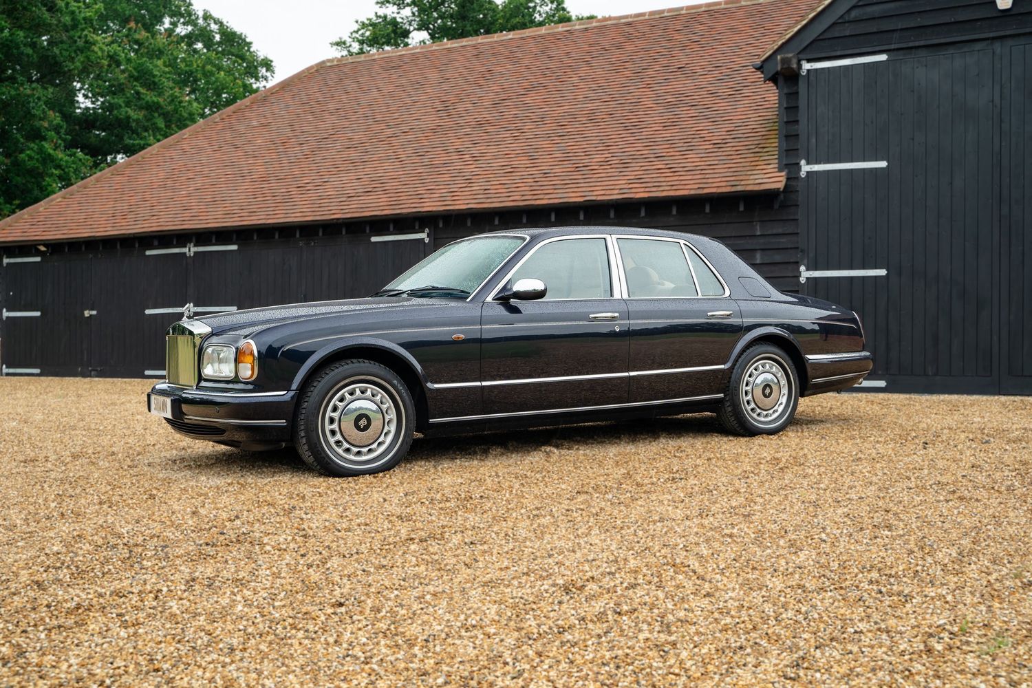 Side view of vintage luxury sedans parked by black barn structure.