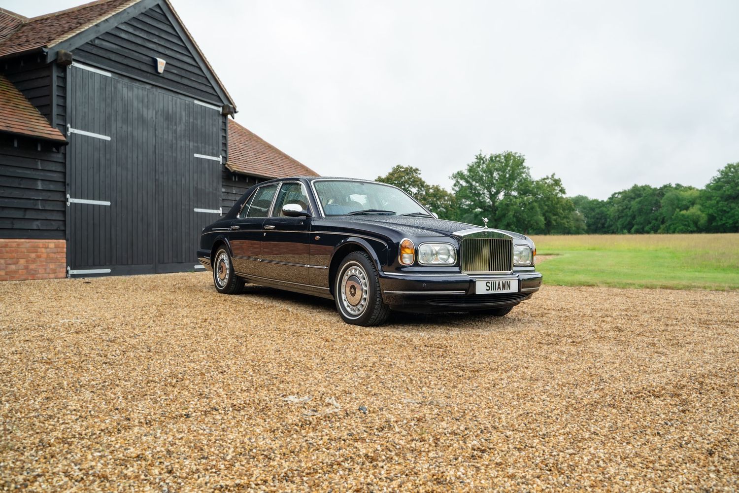 Wide shot of a black barn building with luxury cars parked on gravel driveway.