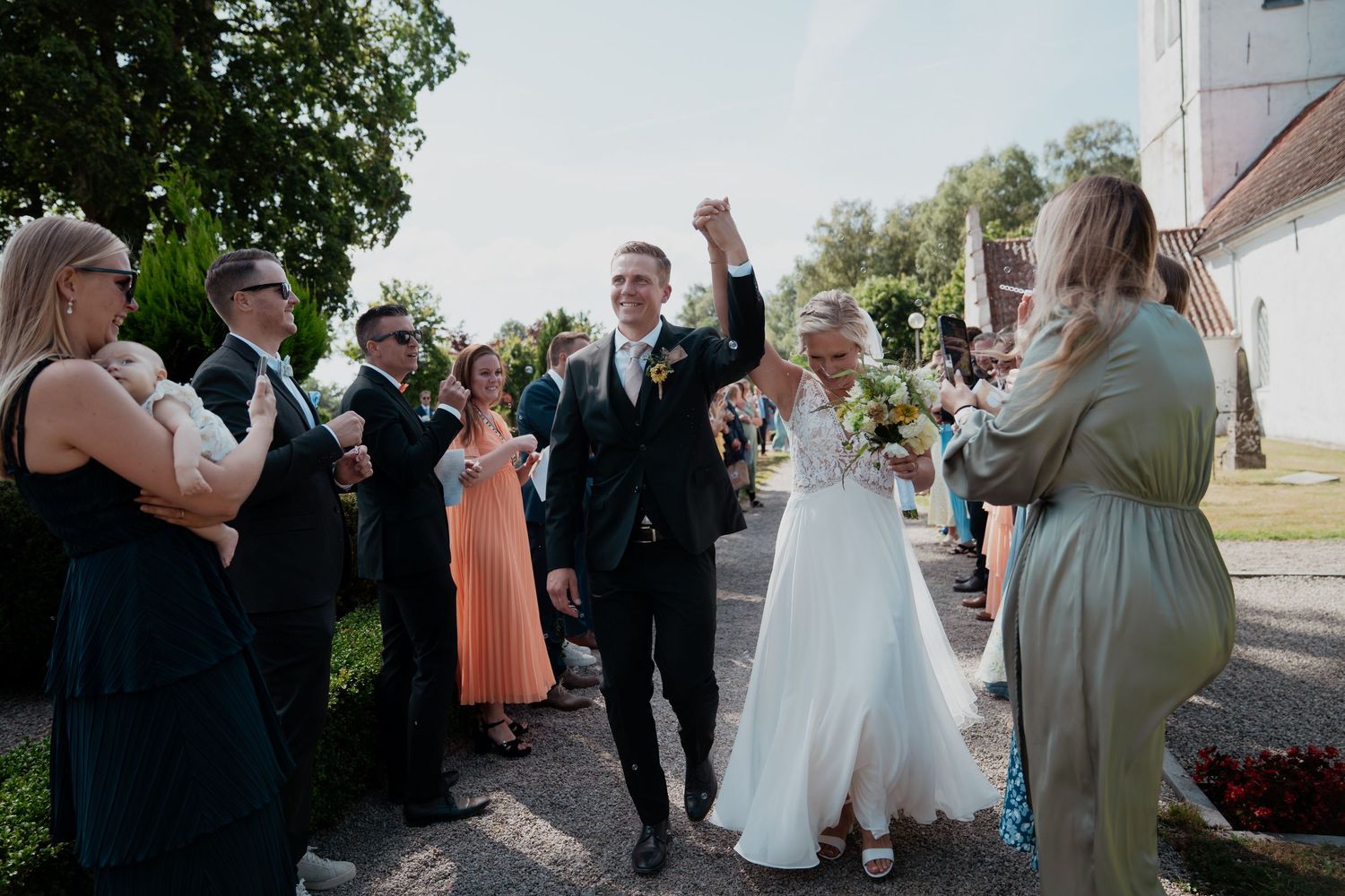 Celebratory outdoor wedding scene with guests gathering around a white church building.