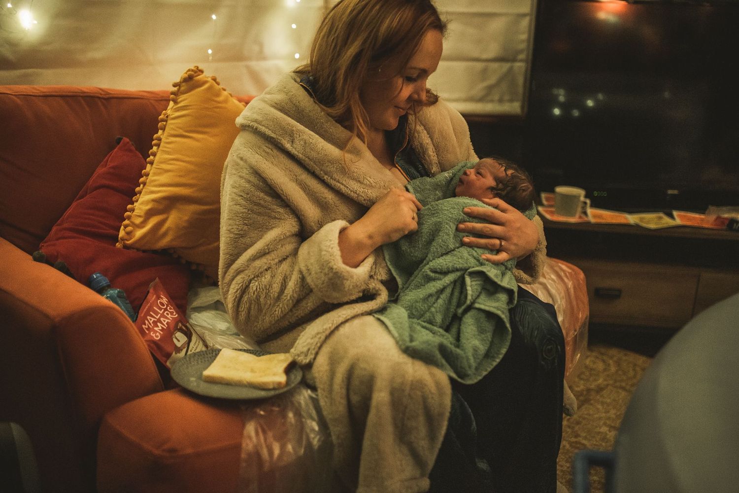 mom holding newborn baby and eating toast