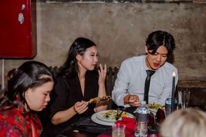 A group of people enjoy a dinner party together at a rustic table setting with plates of food and drinks.