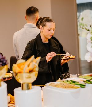 Adult wearing black clothing takes a bite of food while dining at an elegant restaurant table.