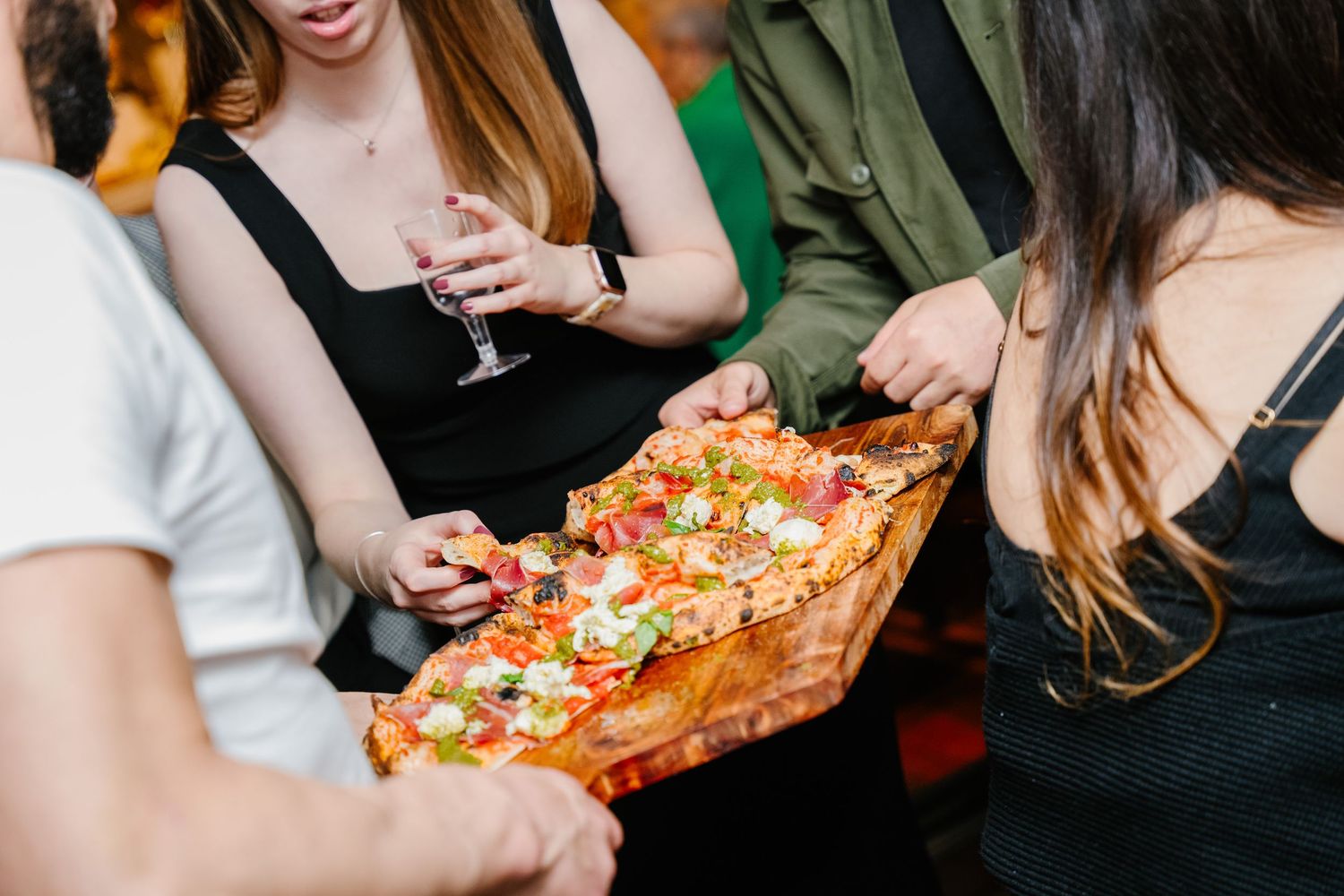 Friends sharing personal pizzas and drinks while socializing and laughing together at a casual gathering.
