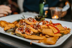 A plate of loaded french fries topped with melted cheese, crispy bacon bits, and drizzled sauce in dim restaurant lighting.