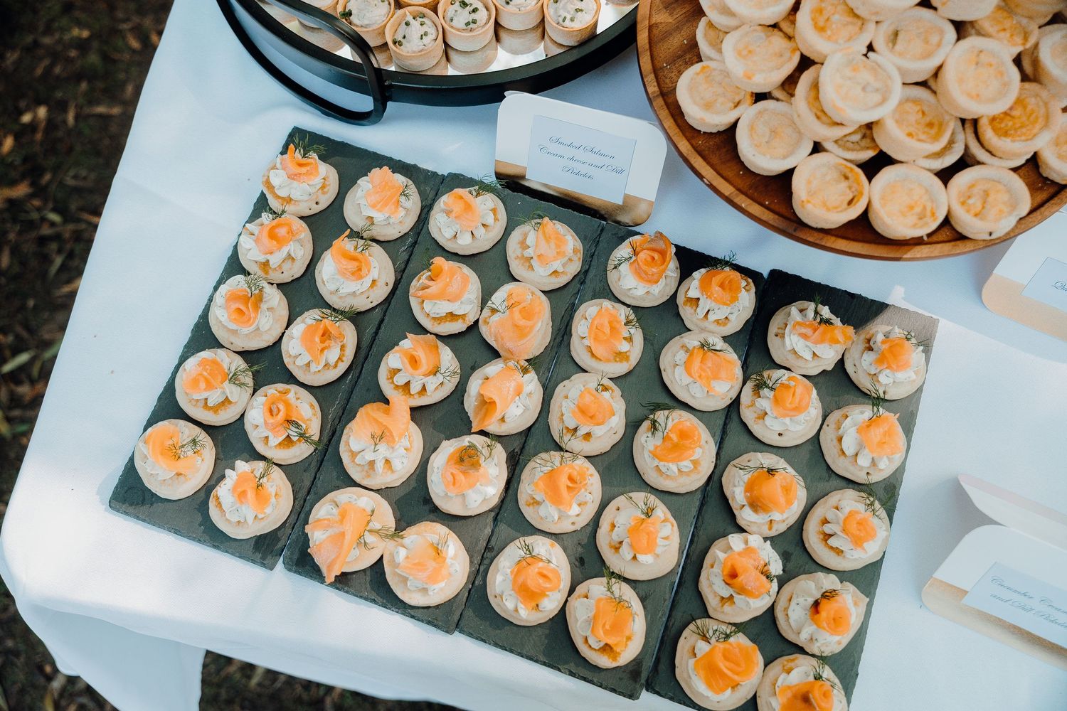 Rows of delicate mini cupcakes with orange-colored frosting arranged neatly on white serving trays at a catering event.
