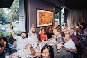 A lively group enjoying dinner and conversation at a restaurant table with framed artwork on the wall.
