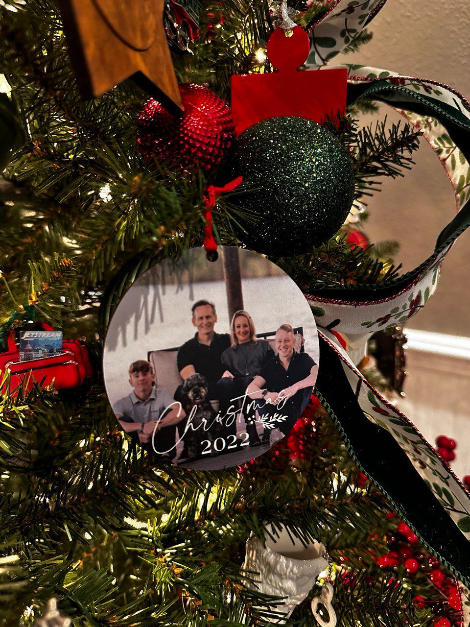 Glittery black and red Christmas ornaments with red ribbons hanging on an illuminated evergreen tree.