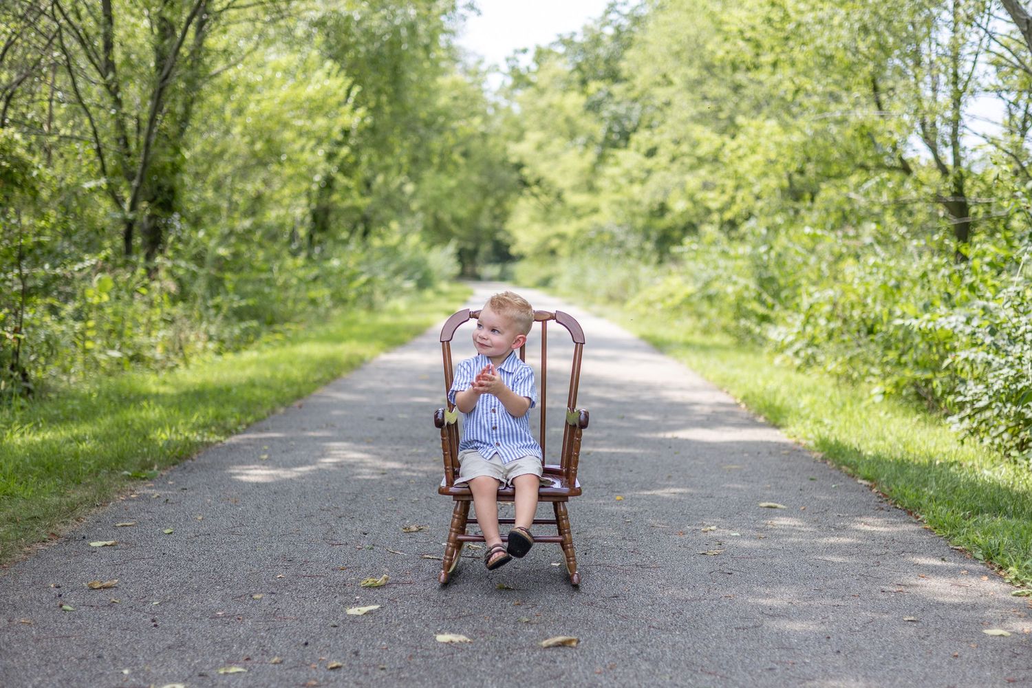 Springfield, IL Photographer captures a boy clapping while sitting on a chair in a trail during a milestone session in Central, IL