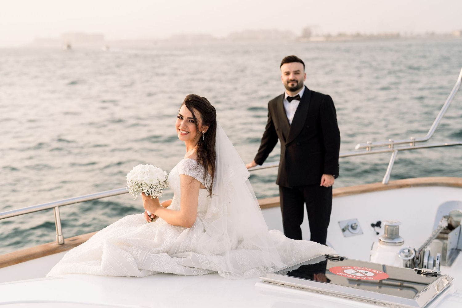 A bride and groom share a romantic moment on a boat deck with water views in the background.