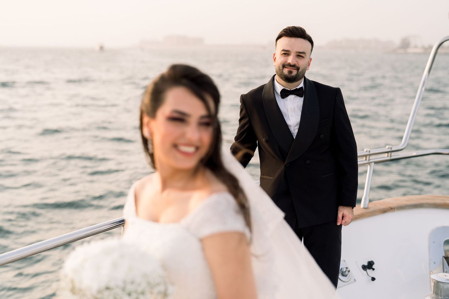 A couple standing on a luxury yacht deck during a romantic golden hour sunset.