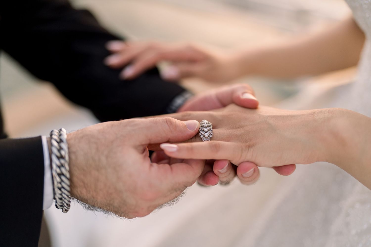 Two hands meeting in a loving grasp as one places a ring on the other's finger during what appears to be a proposal.